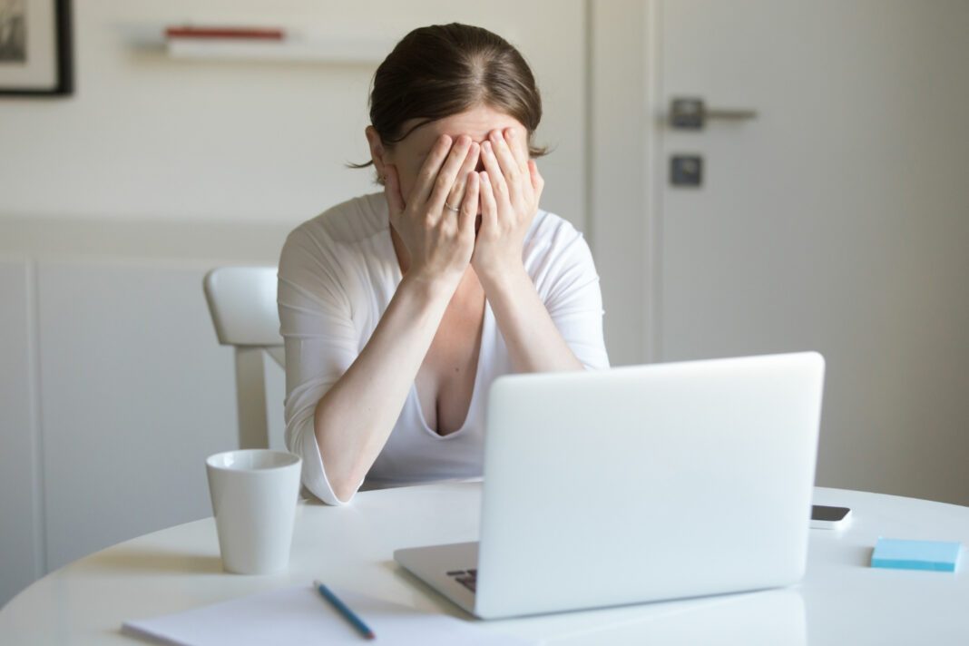 portrait-of-woman-at-the-desk-with-laptop-hands-closing-face