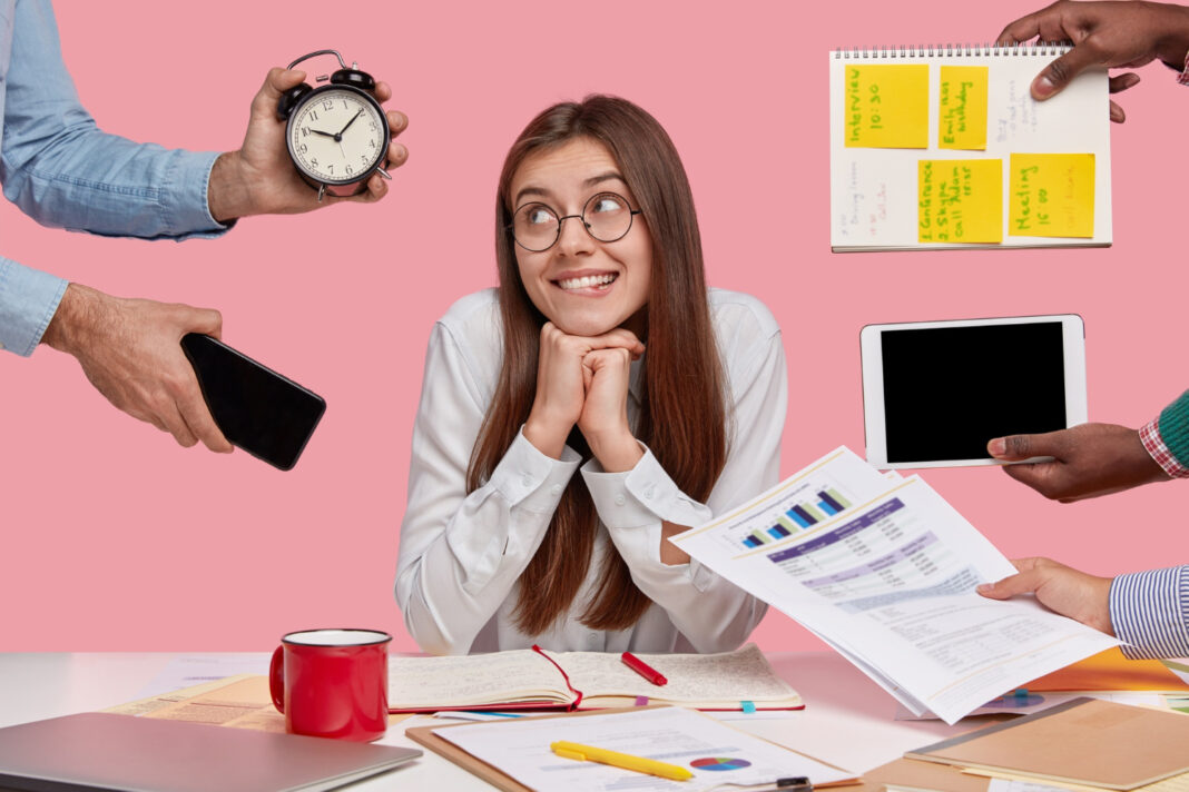 brunette-woman-sitting-at-desk-surrounded-with-gadgets-and-papers